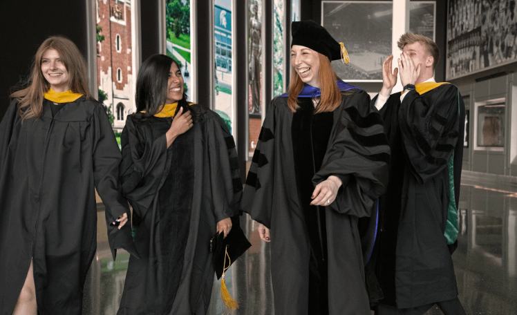 Four graduate students wearing caps and gowns laughing