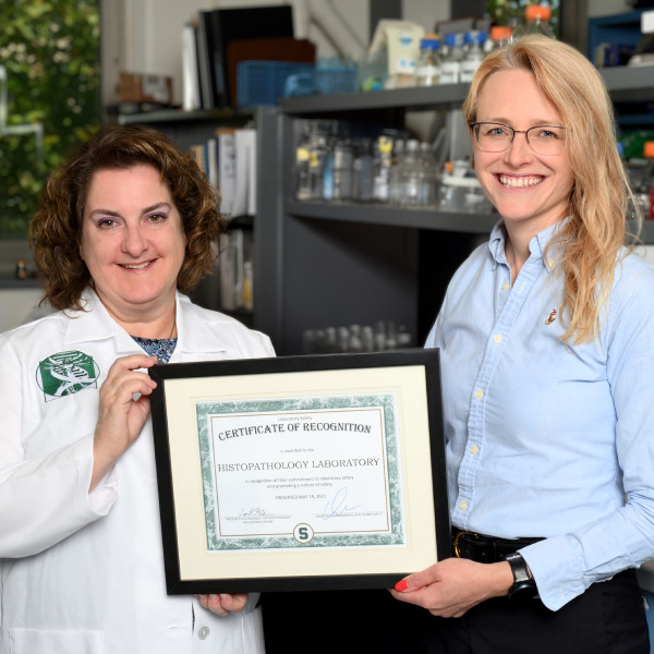 Two people holding up a certification for the histopathology lab