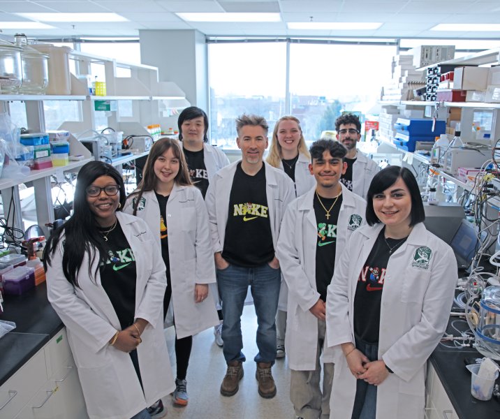 Group photo of students and a professor wearing lab coats surrounded by lab equipment