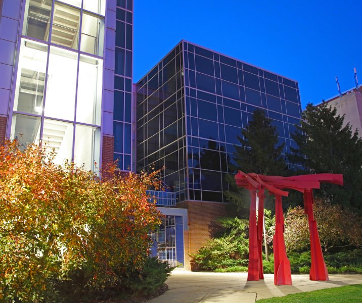 photo of the physiology building at night with a red metal sculpture in the foreground